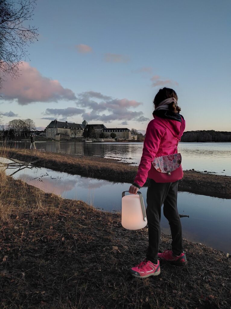 A young girl holding a lantern in front of the pond and Paimpont Abbey